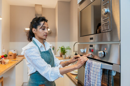 Focused Woman Adjusting Oven Settings In Kitchen