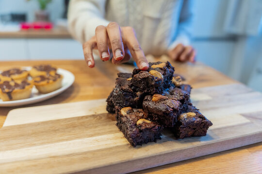 Close-Up Of Hand Reaching For Brownies On Cutting Board