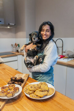 Smiling Woman Holding Dog In Cozy Kitchen