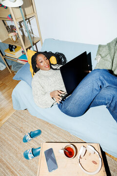 Woman at home chilling on couch using laptop smiling. Direct flash