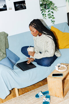 Woman at home sitting on couch using laptop. Direct flash