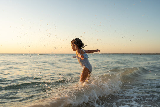 A little toddler smiling and jumping in the water at sunset.