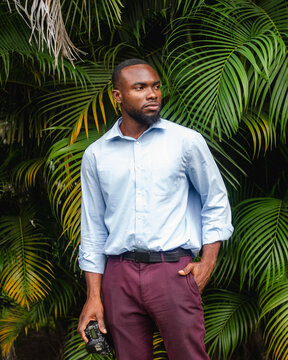 Man stands in front of palm trees holding camera