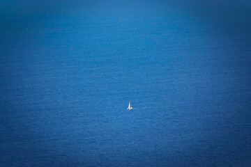 Obraz premium A lone white sailboat sails across vast deep blue Mediterranean Sea in gentle wind. A recreational vessel cruises the open sea and explores picturesque coastlines of western Sicily in sunny springtime