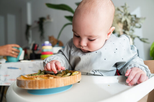 Baby eating broccoli and vegetables from wooden plate