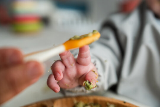 Parent feeding baby with broccoli puree on orange spoon