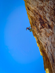 LOW ANGLE VIEW: Experienced female climber in the middle of a limestone tufa line. Young woman is lead climbing a challenging overhang. Adrenaline sports activities in western part of sunny Sicily.