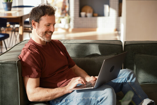 Happy man browsing on laptop sitting in couch