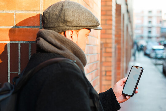 Man in Flat Cap Leaning Against Wall Using Smartphone City Street