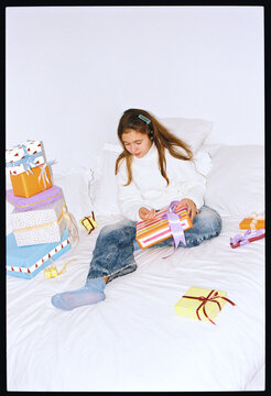 Child opening gifts on a cozy bed in a festive setting