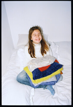 Smiling girl folding colorful clothes in cozy bedroom setting
