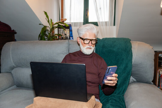 Senior Man Using Laptop and Smartphone on Couch