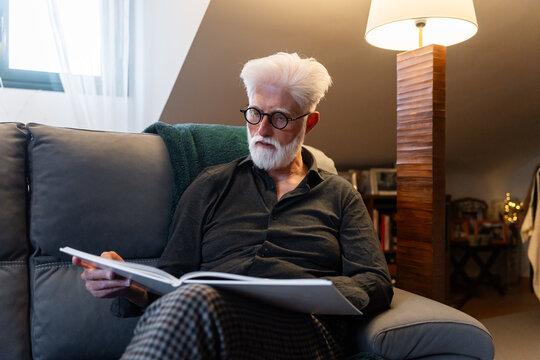 Elderly Man Reading Book On Couch
