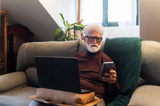 Elderly Man Using Smartphone and Laptop at Home
