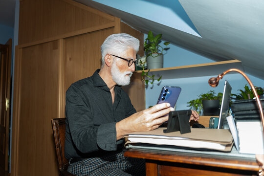 Senior Man Using Smartphone And Laptop At Desk