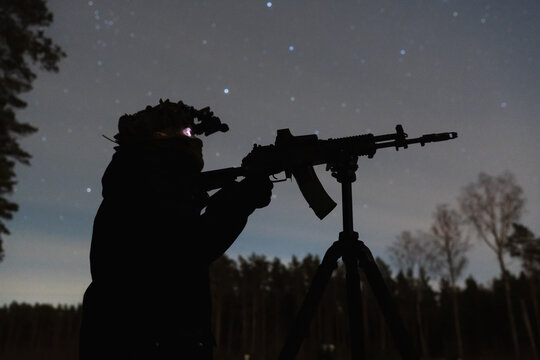 Silhouette of a soldier with night vision device and assault rifle on a tripod against the starry sky at night