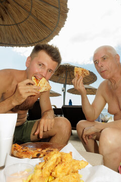 two men eating pizza on the beach