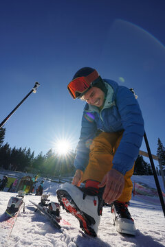 One day of skier in ski resort.
The man smiling and fixing boots