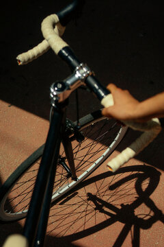 Cyclist holding handlebars of a road bike with shadow on pavement