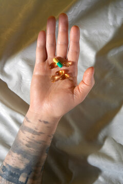 Tattooed hand holding pills in sunlight. Studio shot with copy space