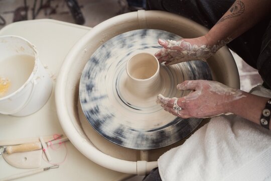 Hands shaping clay on spinning pottery wheel  
