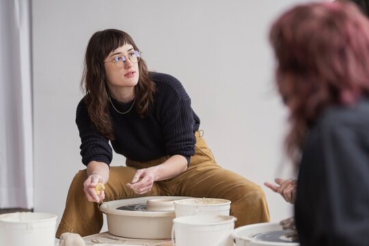 Pottery instructor guiding student at wheel  
