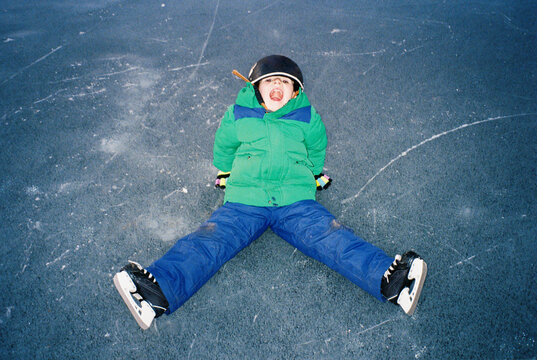 Film portrait of child sitting on frozen pond with ice skates on
