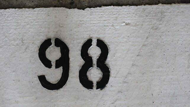 number 98 (Ninety eight) painted in black on the white ground that looks aged and rugged with copy space