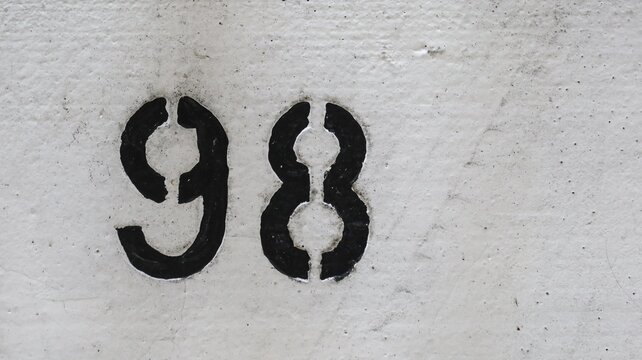 number 98 (Ninety eight) painted in black on the white ground that looks aged and rugged with copy space