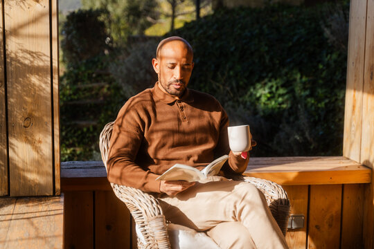 Man Enjoys Quiet Moment with Book and Tea on Sunny Log Cabin Balcony