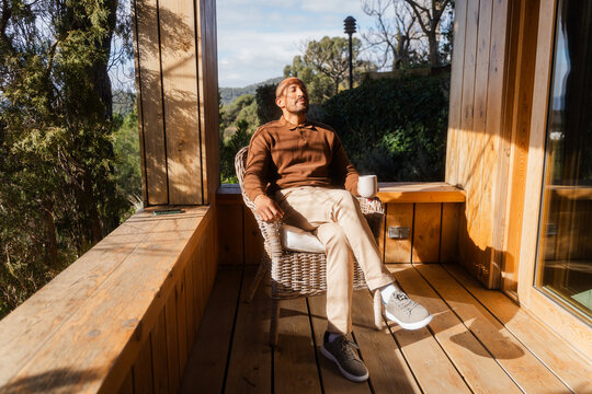Man Relaxing with Tea on Log Cabin Balcony on Sunny Day