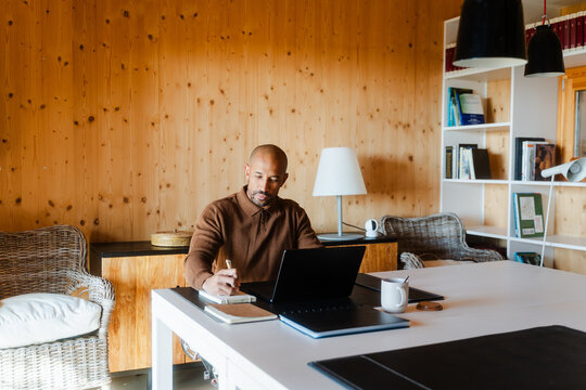 Entrepreneur Taking Notes at Office Desk with Laptop and Coffee
