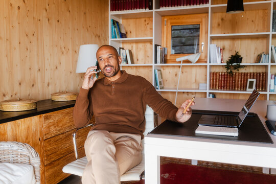 Businessman Talking on Phone in Home Office with Laptop and Bookshelf