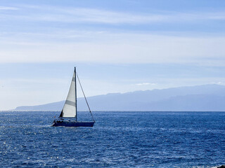 Fototapeta premium Sailing boat floating in clear blue water near rocky shore during bright sunny day in Los Gigantes Tenerife