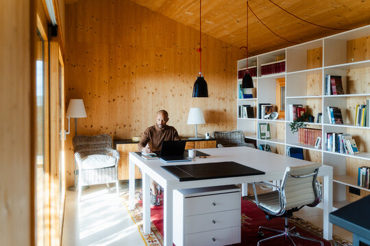 Thoughtful Entrepreneur Working with Laptop and Notepad in Log Cabin