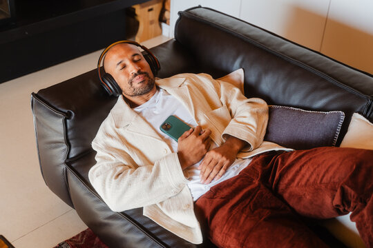Man Relaxing on Sofa, Enjoying Music on Phone in Cozy Log Cabin