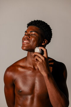 Smiling Shirtless Man Using Skincare Device