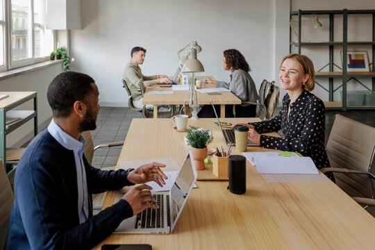 Coworkers collaborating and using laptops in modern office