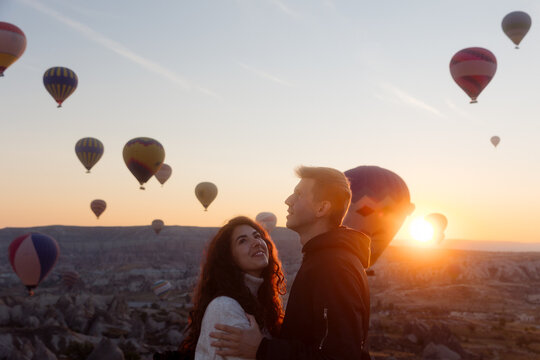 Young couple hugging against backdrop of balloons taking off.