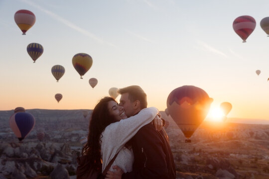 Young couple hugging against backdrop of balloons taking off.