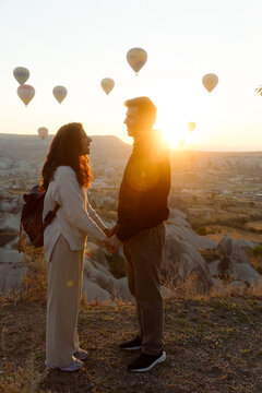 A young couple stands against a backdrop of rising hot air balloons.