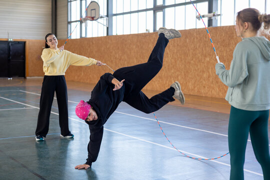 Young man training handstand with two girls holding skip ropes 