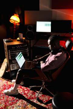 Man Editing Music Working on Laptop  in a Cozy Studio