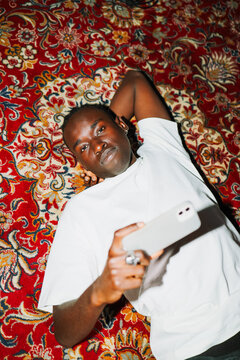 Portrait Man lying on patterned rug with phone by flash