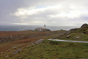 Neist Point Lighthouse on the Isle of Skye, Scotland; iconic historic coastal beacon atop dramatic sea cliffs in the Scottish Highlands, meandering pathway toward lighthouse in autumn landscape