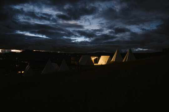 Illuminated teepees glowing under dramatic cloudy sky at night