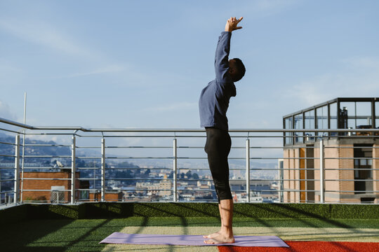 Man practicing yoga on rooftop with city view in background