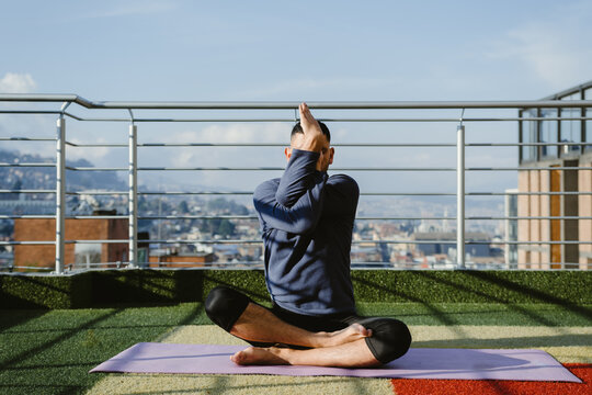 Man practicing yoga eagle pose on rooftop with city view