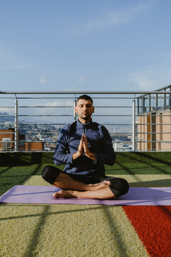 Young man meditating on rooftop with city view in background