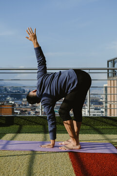 Man practicing standing half forward bend yoga pose on rooftop